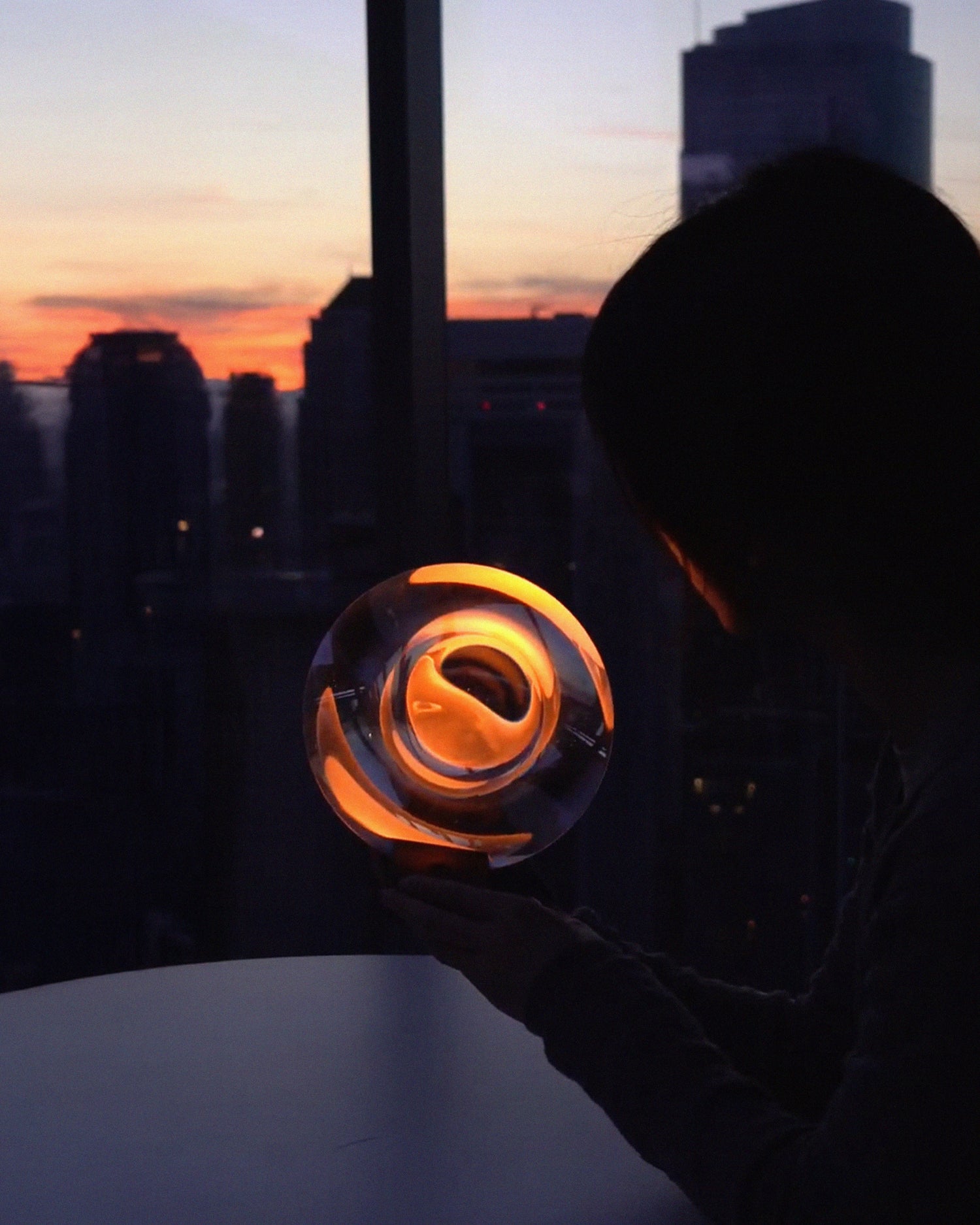 Person holding a glowing object dream sailor table lamp against a cityscape at sunset