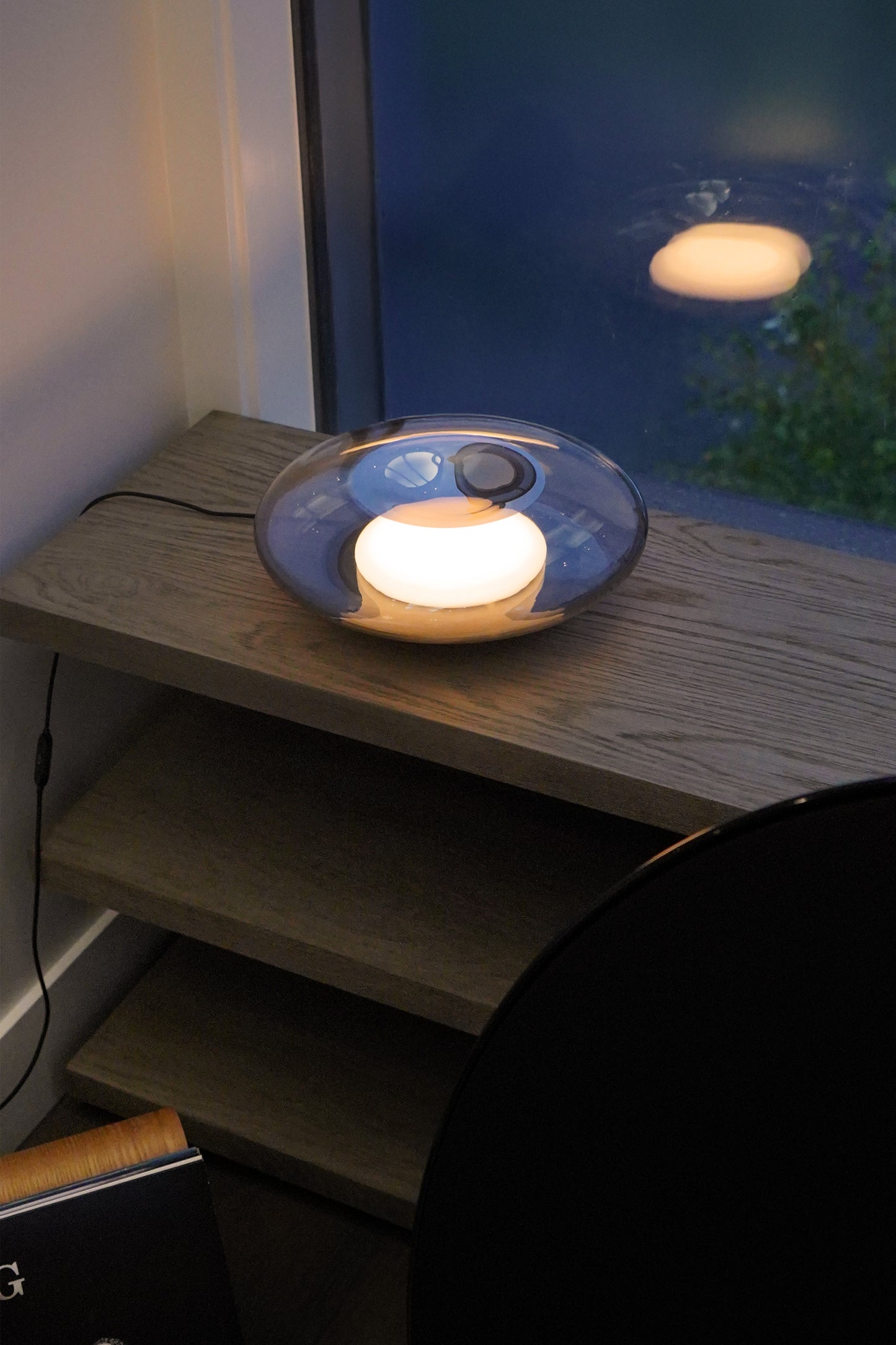 Round light fixture on a wooden surface with a blurred outdoor scene in the background