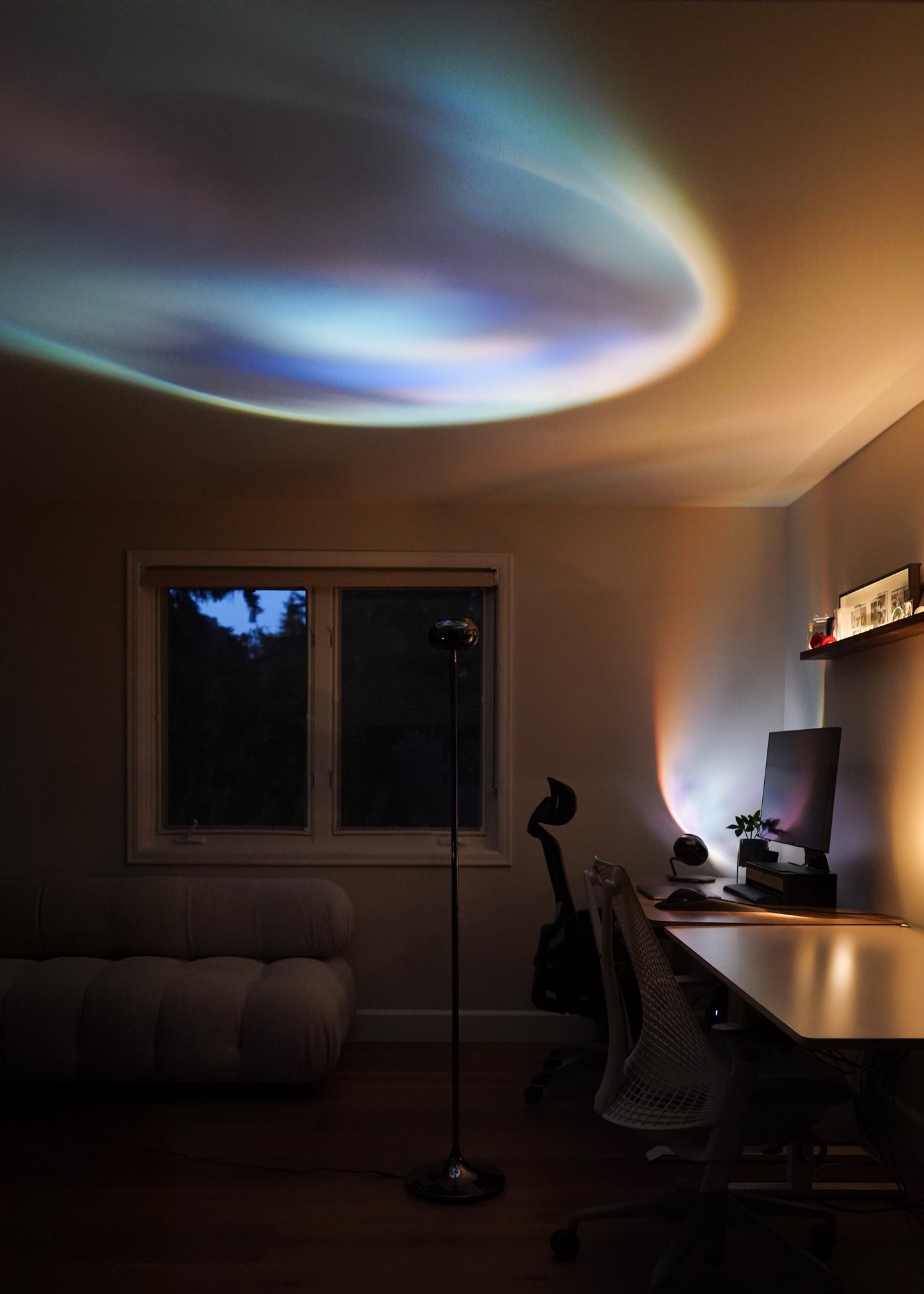 Room interior with a desk and computer setup, featuring a colorful light projection on the ceiling.