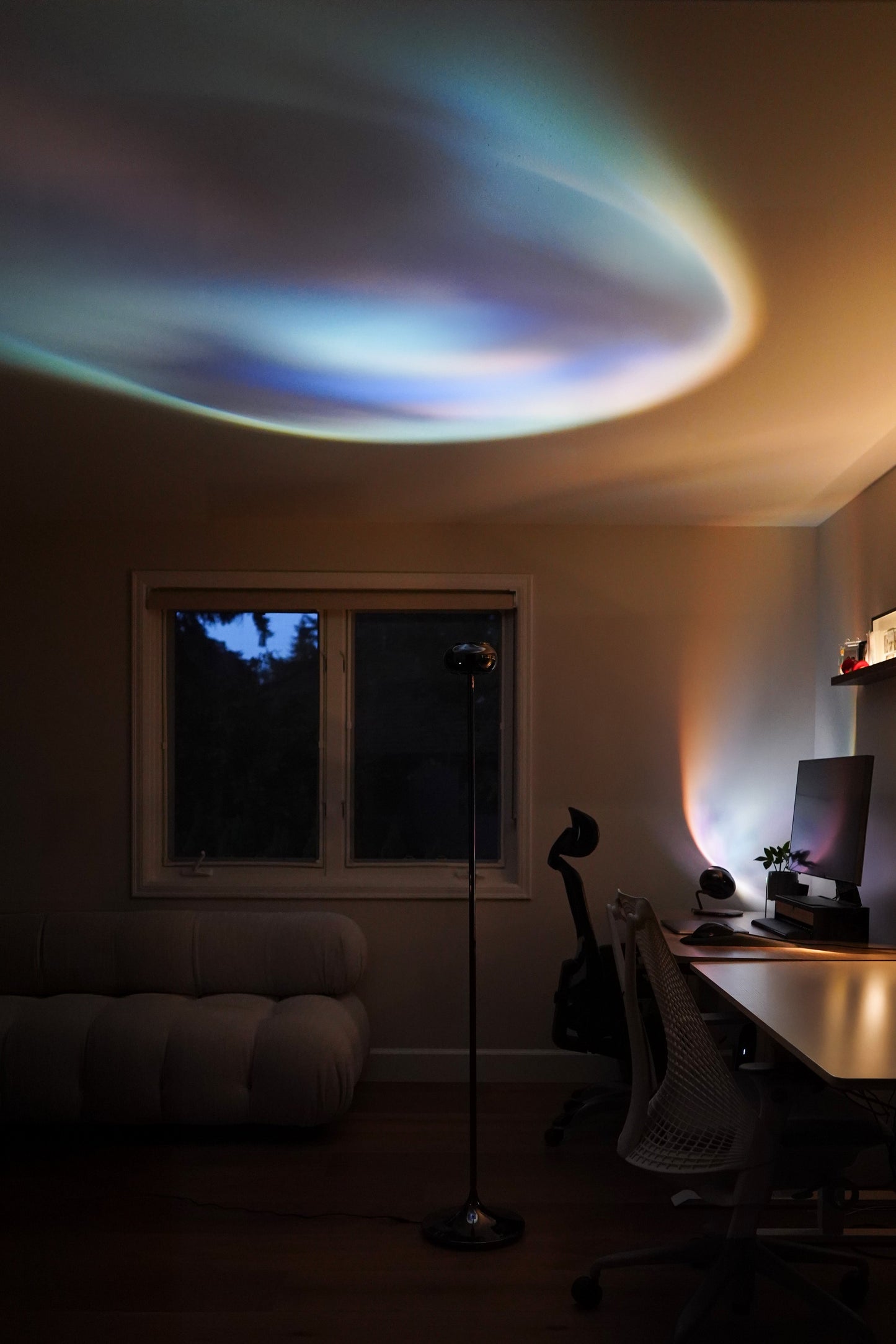 Room interior with a desk and computer setup, featuring a colorful light projection on the ceiling.