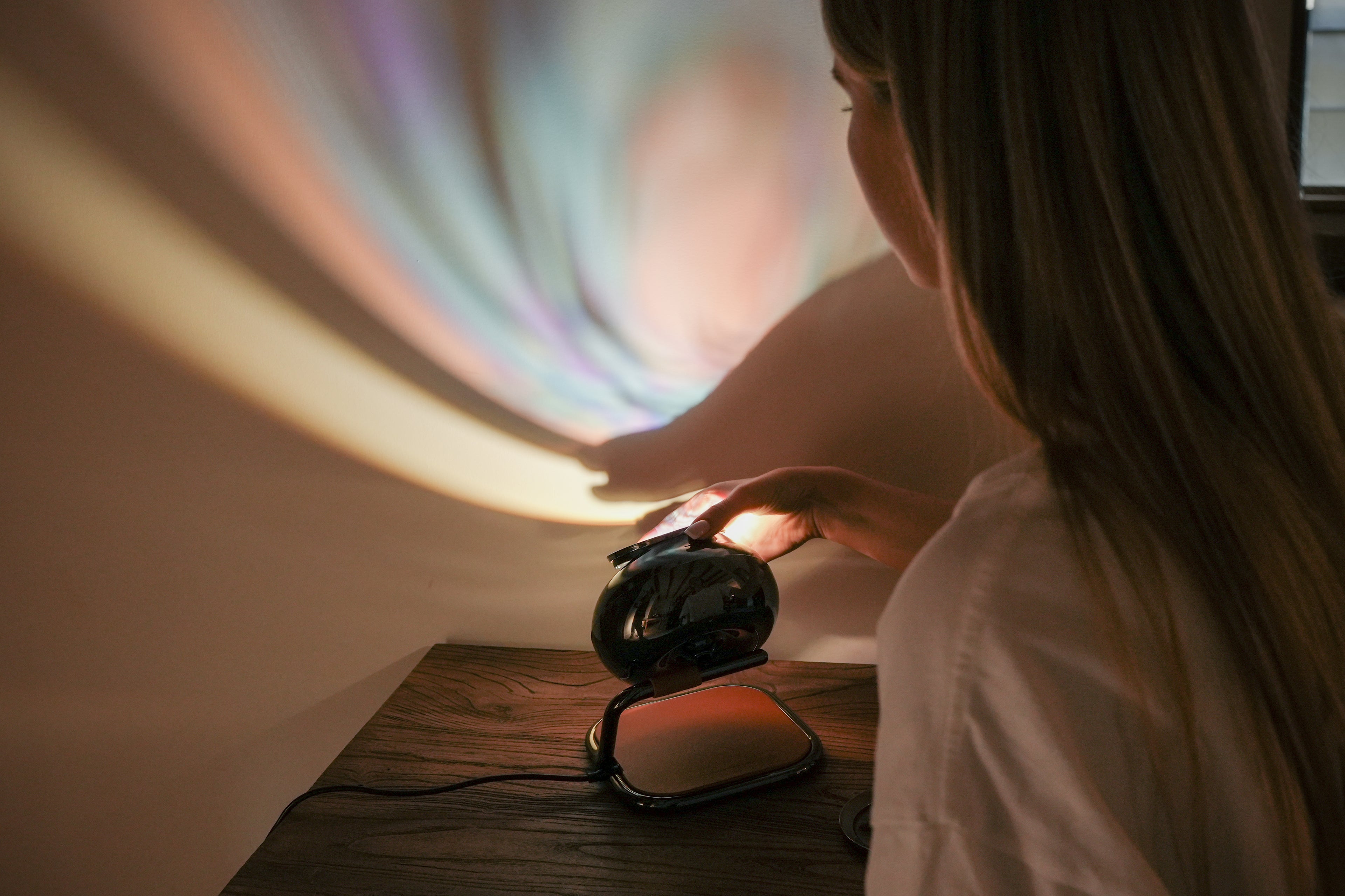 Person interacting with a small device emitting colorful light patterns on a wall.