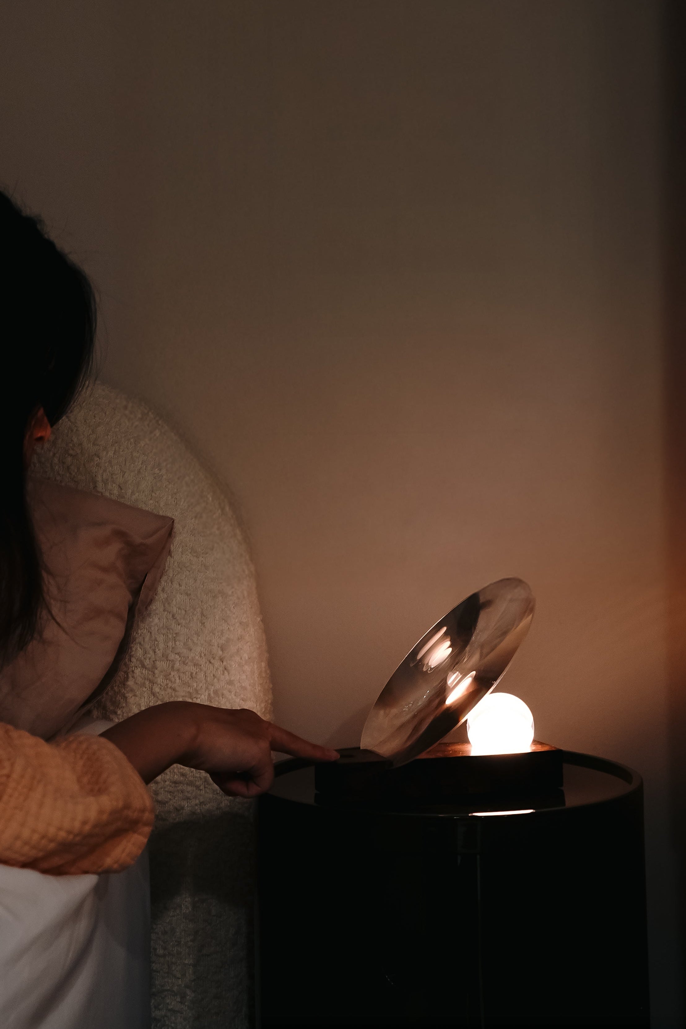 Person using a lamp on a bedside table in a dimly lit room