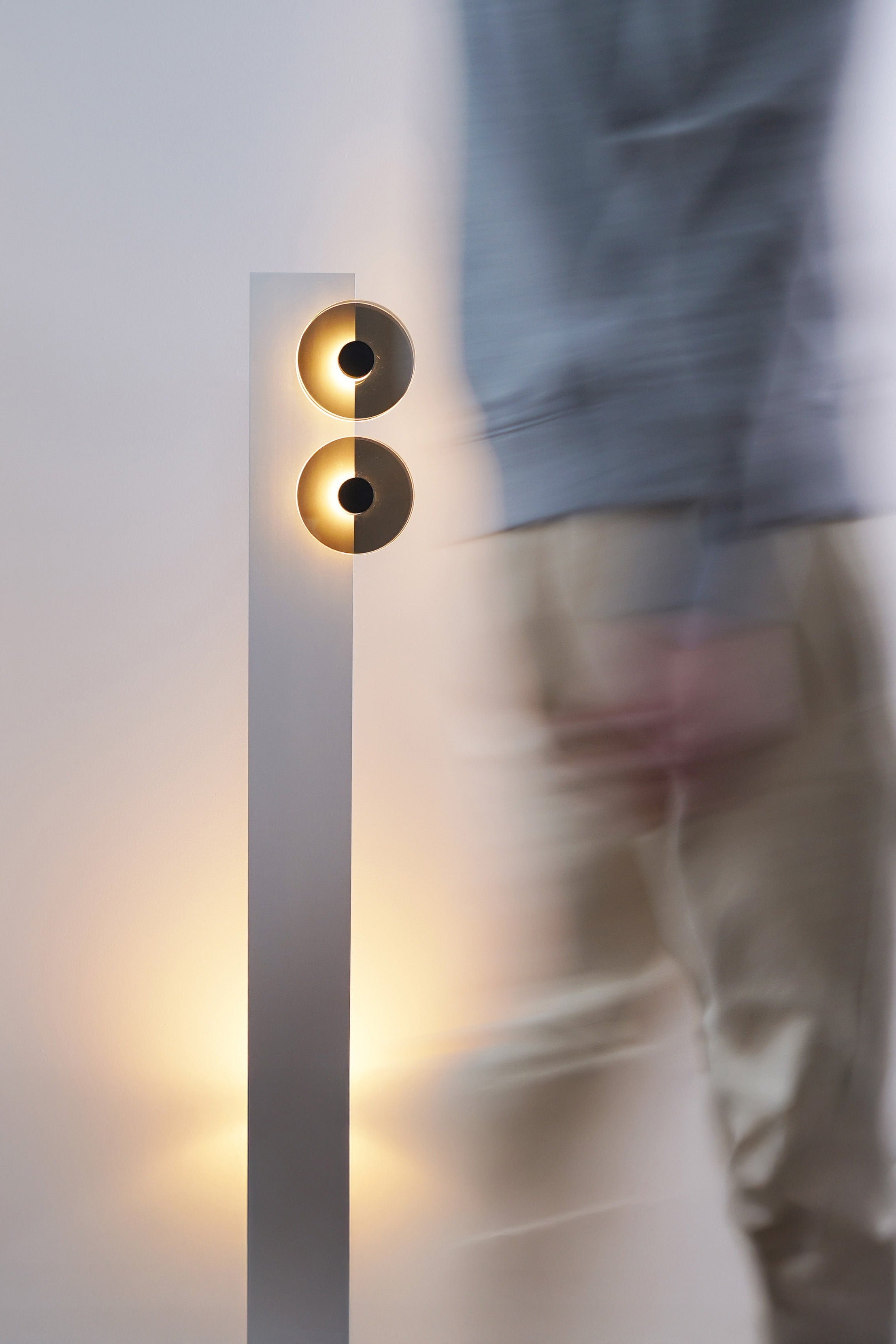 Person standing in front of a modern wall-mounted light fixture with a blurred background