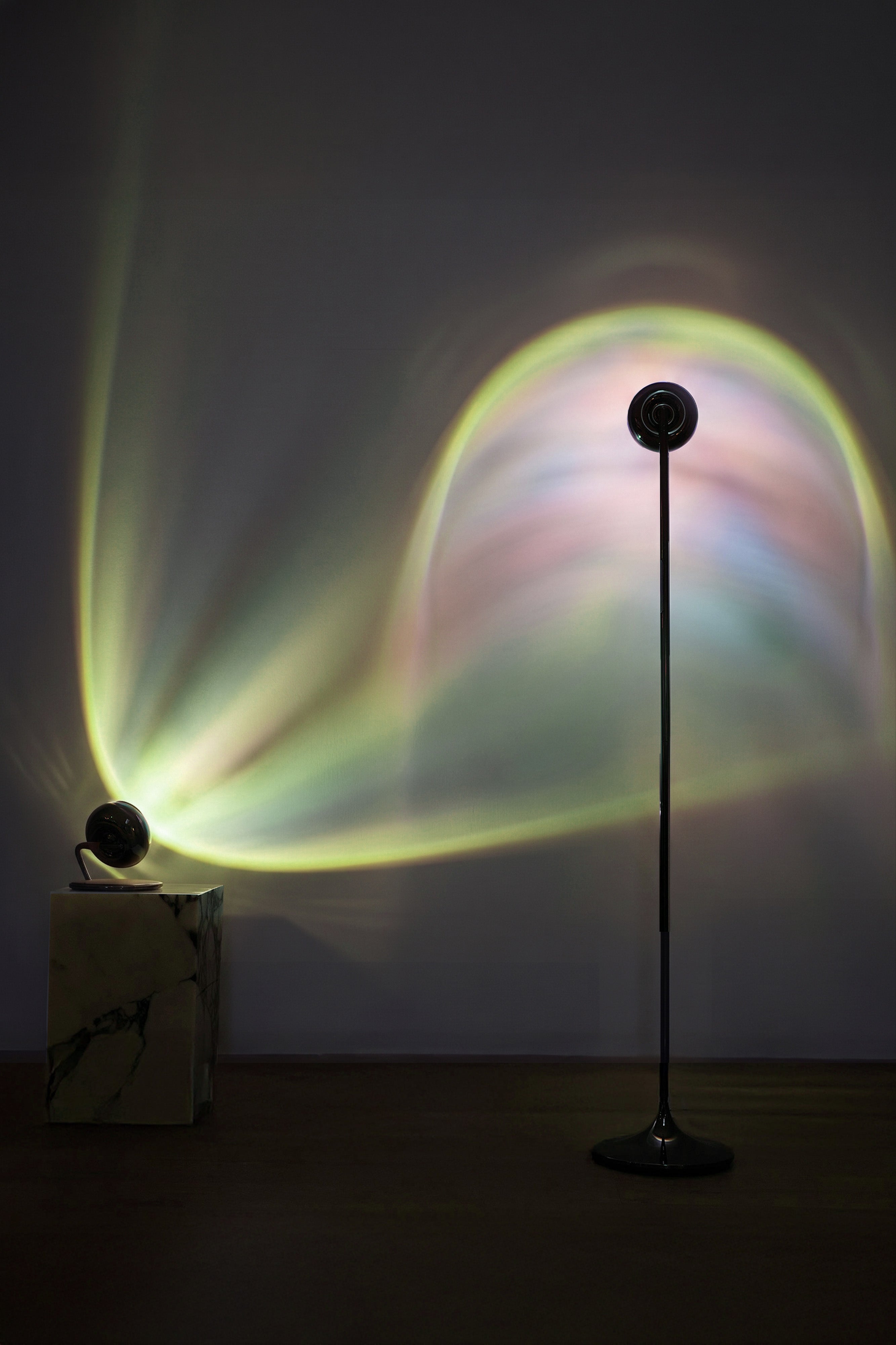 Colorful light projection on a wall with a standing lamp in a dark room.