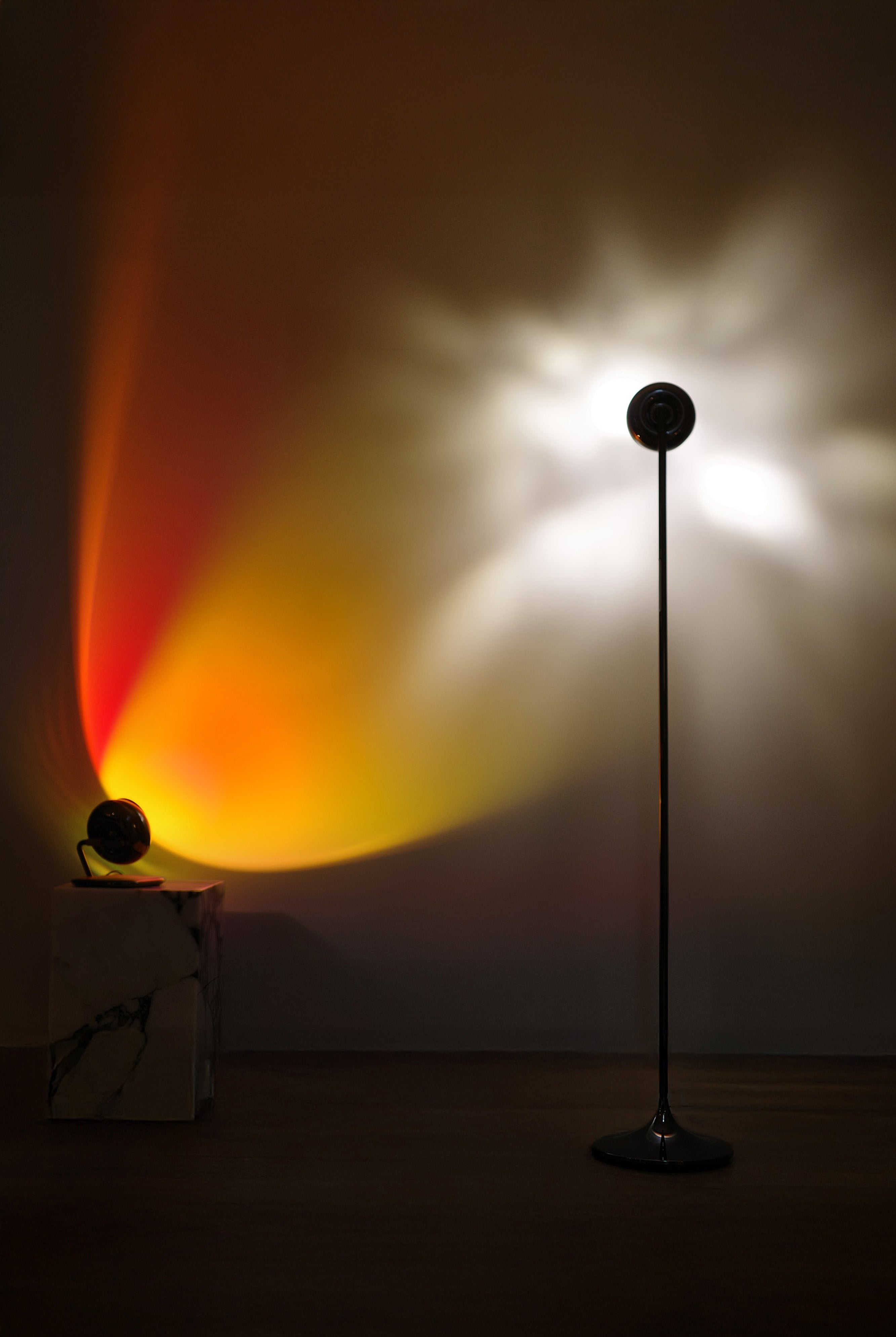 Two floor lamps casting colorful light patterns on a wall in a dark room.