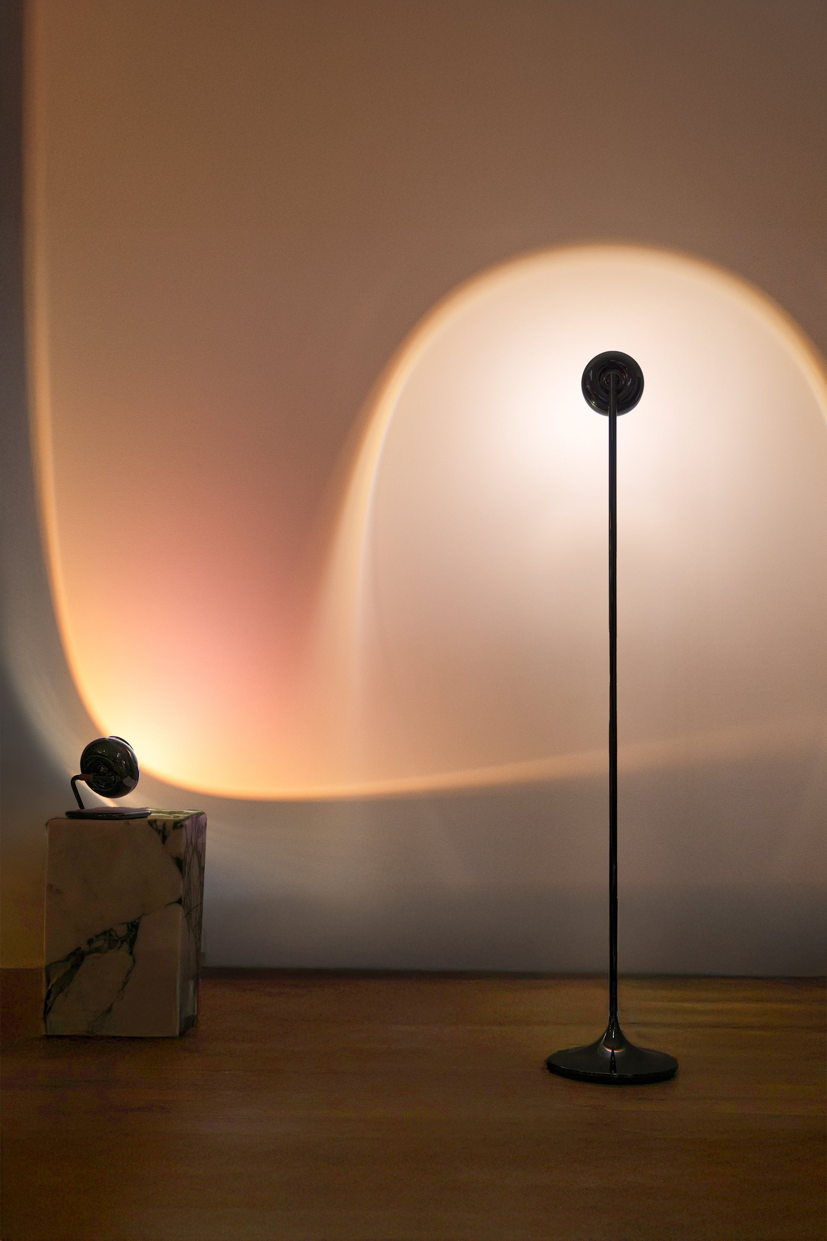 Floor lamp casting a warm glow on a wall with a minimalistic design.